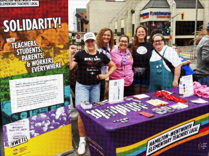 Photo of HWETL members at a public even standing together behind a table and by a banner branded with HWETL's logo and messaging.
